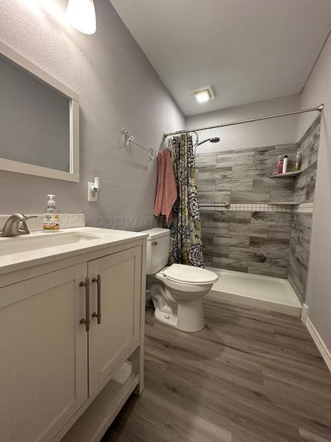 full bath featuring wood finished floors, toilet, vanity, and tiled shower