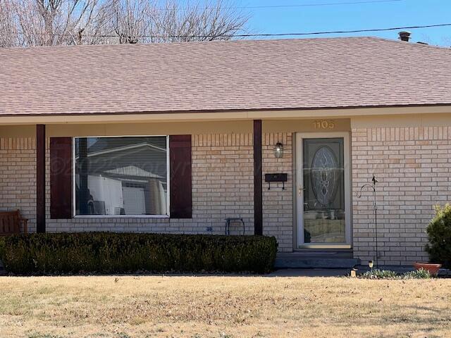 view of front of property featuring roof with shingles, a front yard, and brick siding