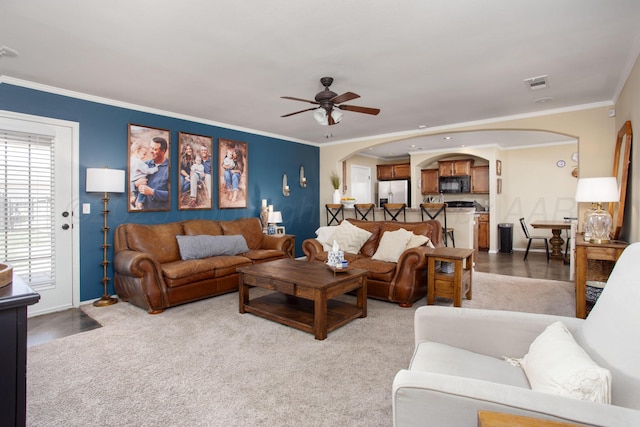 living area featuring ceiling fan, visible vents, arched walkways, baseboards, and ornamental molding