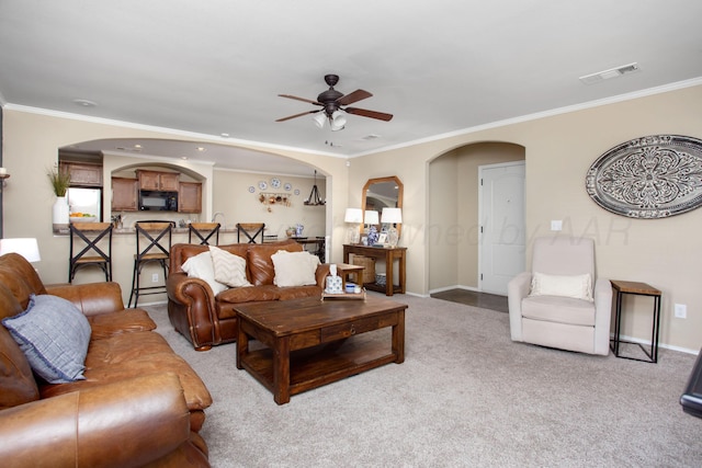 living room with crown molding, light carpet, baseboards, ceiling fan, and arched walkways