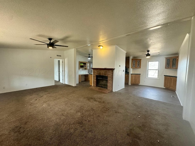 unfurnished living room featuring visible vents, a fireplace, dark carpet, a textured ceiling, and a ceiling fan