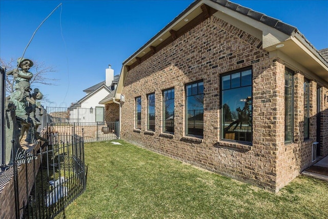 view of home's exterior featuring brick siding, fence, and a lawn