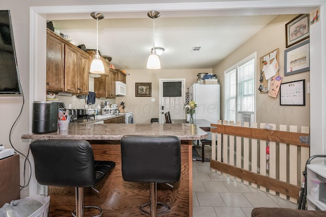 4114 S Hayden St, Amarillo, TX 79119 - kitchen with white microwave, brown cabinets, a breakfast bar area, a peninsula, and hanging light fixtures