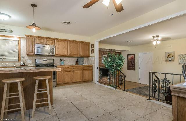 3406 Patterson Dr, Amarillo, TX 79109 - kitchen featuring appliances with stainless steel finishes, ceiling fan, backsplash, a breakfast bar, and hanging light fixtures