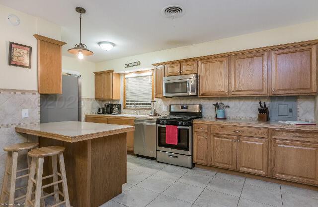 3406 Patterson Dr, Amarillo, TX 79109 - kitchen featuring appliances with stainless steel finishes, a breakfast bar, a peninsula, brown cabinets, and light countertops