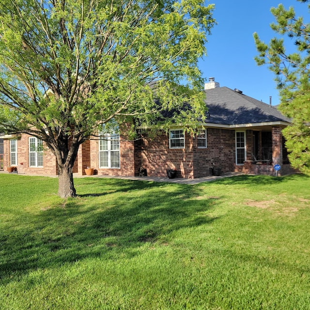 rear view of property with brick siding, a yard, and a chimney