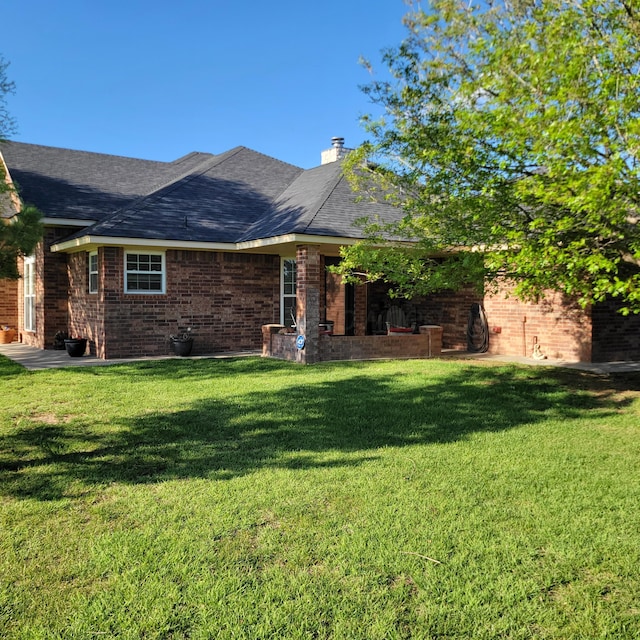 exterior space with a yard, a shingled roof, and brick siding