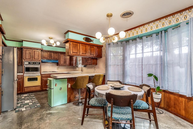 kitchen with backsplash, appliances with stainless steel finishes, wooden walls, hanging light fixtures, and a chandelier