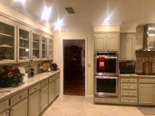 kitchen with black electric cooktop, wall chimney exhaust hood, light tile patterned floors, stainless steel double oven, and crown molding