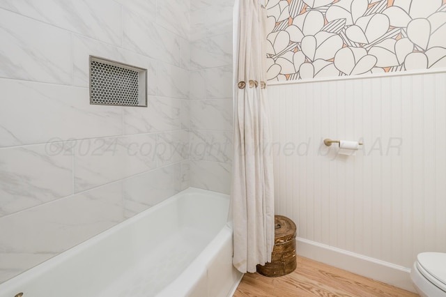 full bath with toilet, shower / bath combo with shower curtain, wood finished floors, and baseboards