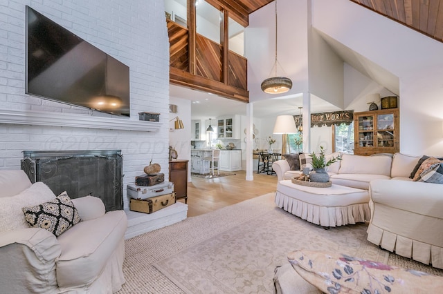 living room featuring high vaulted ceiling, a brick fireplace, and wood finished floors