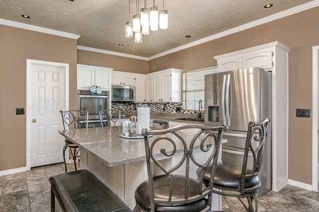 kitchen with appliances with stainless steel finishes, white cabinets, a breakfast bar area, decorative backsplash, and a sink