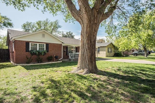 ranch-style home with covered porch, brick siding, fence, and a front lawn