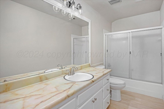 bathroom featuring visible vents, vanity, wood finished floors, toilet, and enclosed tub / shower combo