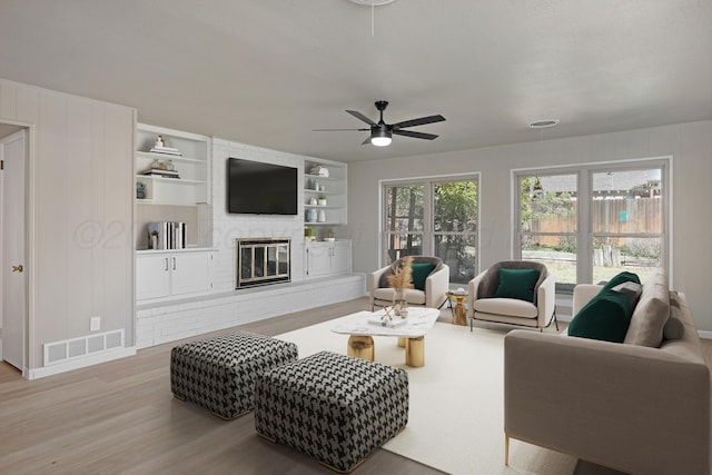 living room featuring ceiling fan, visible vents, a brick fireplace, baseboards, and light wood finished floors