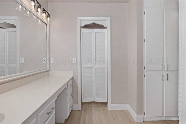 bathroom with vanity, baseboards, a textured wall, and wood finished floors