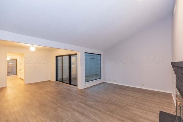 unfurnished living room featuring lofted ceiling, light wood-style flooring, a brick fireplace, and baseboards