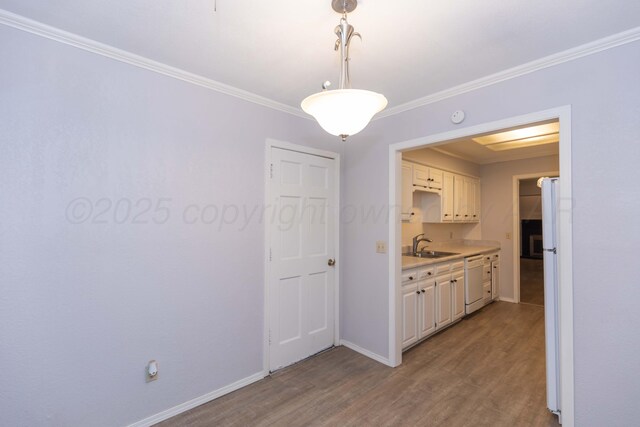 unfurnished dining area with a sink, wood finished floors, ornamental molding, and baseboards