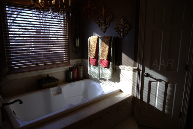 bathroom featuring plenty of natural light, a relaxing tiled tub, and an inviting chandelier