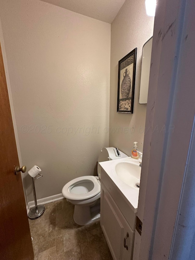 half bathroom featuring stone finish flooring, vanity, baseboards, and toilet
