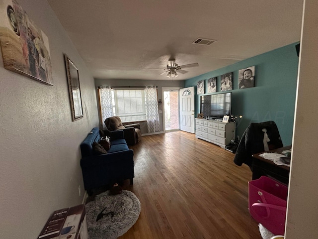 sitting room featuring a textured wall, visible vents, a ceiling fan, and wood finished floors