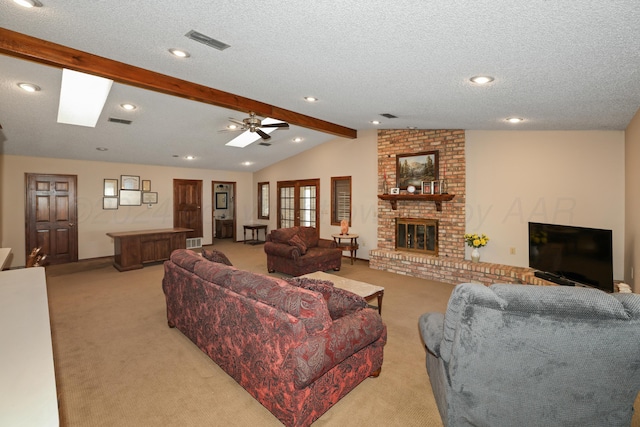 living room with vaulted ceiling with skylight, a textured ceiling, light colored carpet, ceiling fan, and a fireplace