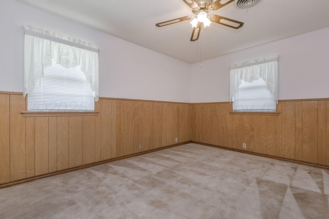 empty room with wainscoting, a ceiling fan, wooden walls, and carpet