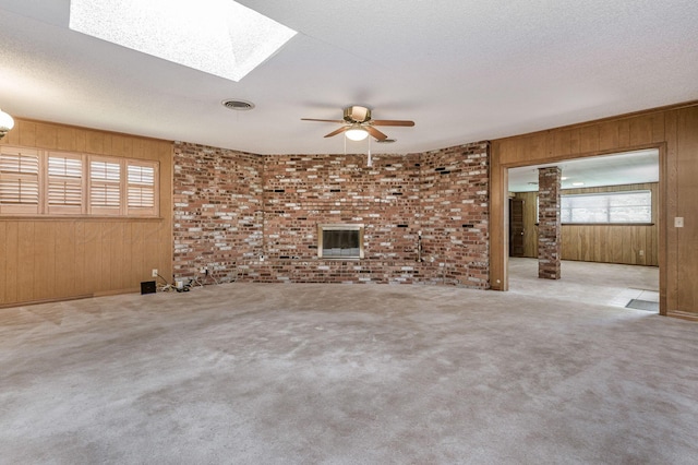 unfurnished living room with wooden walls, ceiling fan, carpet, a skylight, and brick wall