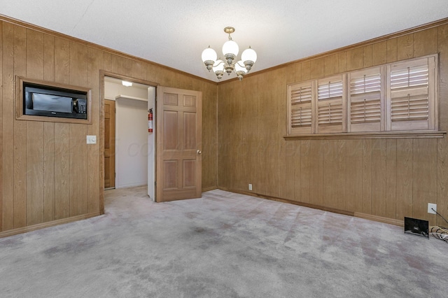 carpeted empty room with a chandelier, wood walls, crown molding, and baseboards