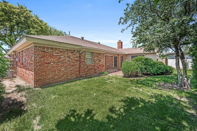 back of property with brick siding, a yard, a chimney, and a shingled roof