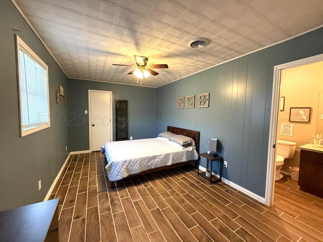 bedroom featuring a ceiling fan, baseboards, visible vents, wood tiled floor, and ensuite bath