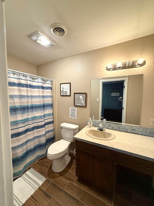 full bath featuring visible vents, toilet, wood tiled floor, a textured ceiling, and vanity