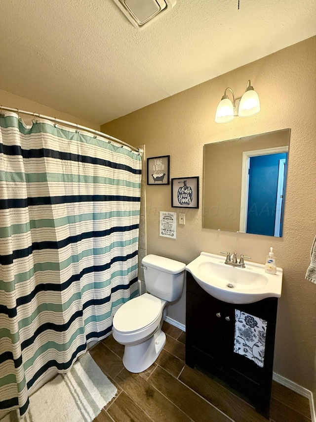 bathroom with a textured ceiling, a textured wall, toilet, vanity, and wood tiled floor