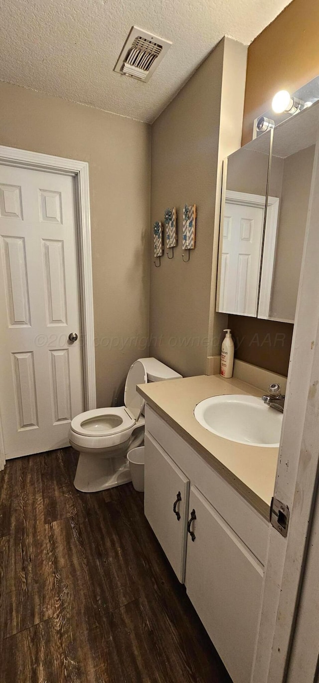 bathroom with wood-type flooring, toilet, vanity, and a textured ceiling