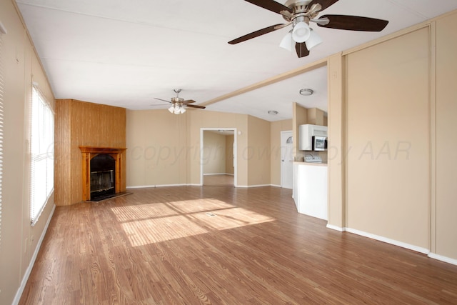 unfurnished living room featuring ceiling fan, light wood-type flooring, a fireplace, lofted ceiling, and baseboards
