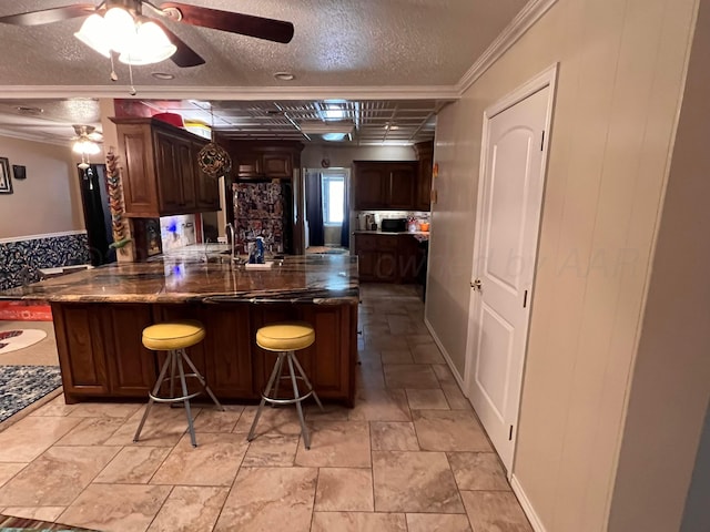 1400 16th St, Hereford, TX 79045 - kitchen featuring a ceiling fan, a textured ceiling, a breakfast bar area, a peninsula, and dark brown cabinets