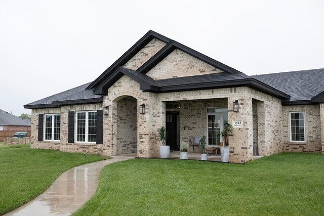 view of front of home with a front lawn, brick siding, and roof with shingles