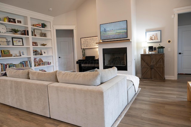 living room with wood finished floors, vaulted ceiling, a fireplace, and baseboards