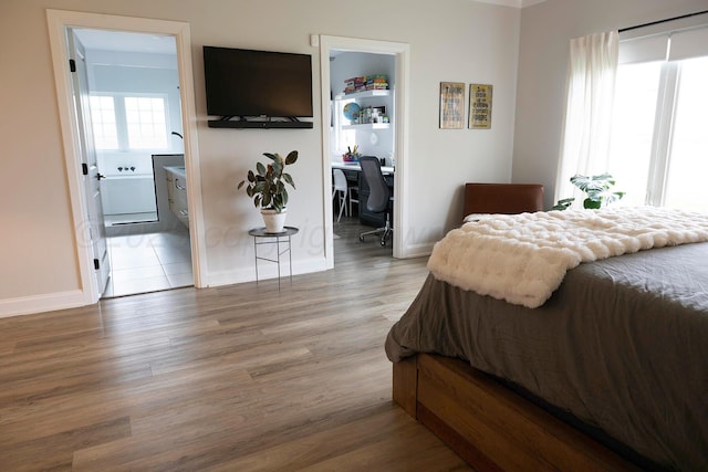 bedroom with wood finished floors, a spacious closet, baseboards, and an office area