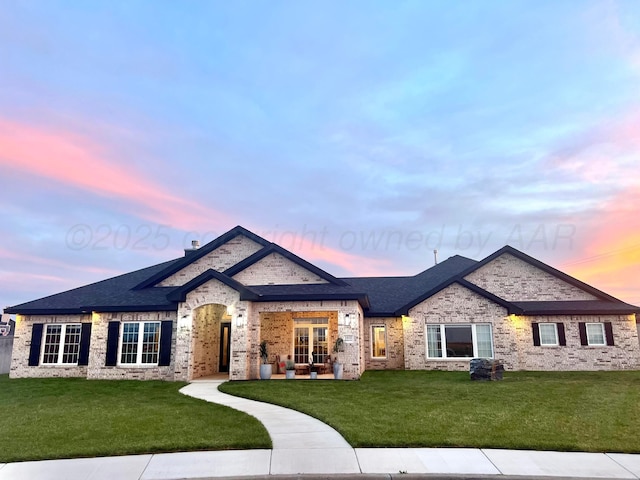 french provincial home featuring a lawn, brick siding, and roof with shingles
