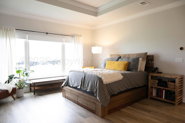 bedroom with wood finished floors, ornamental molding, and a raised ceiling