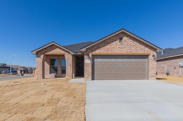 single story home with a shingled roof, concrete driveway, brick siding, and an attached garage