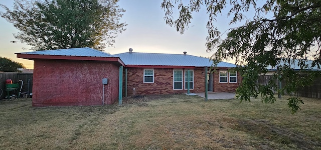 back house at dusk featuring a lawn and a patio area