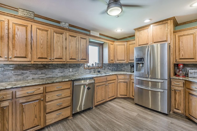 kitchen with decorative backsplash, light stone counters, stainless steel appliances, sink, and light hardwood / wood-style flooring