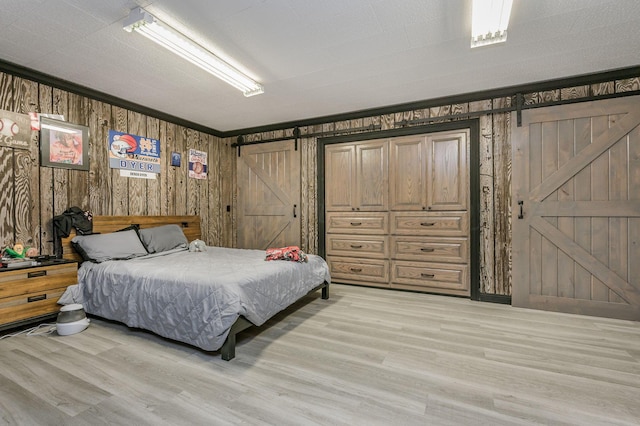 bedroom with wooden walls, a barn door, light hardwood / wood-style floors, and ornamental molding