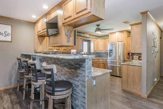 kitchen featuring kitchen peninsula, stainless steel refrigerator with ice dispenser, light brown cabinets, and a breakfast bar area