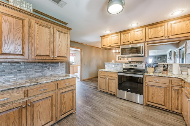 kitchen featuring decorative backsplash, ornamental molding, light hardwood / wood-style floors, light stone counters, and stainless steel appliances