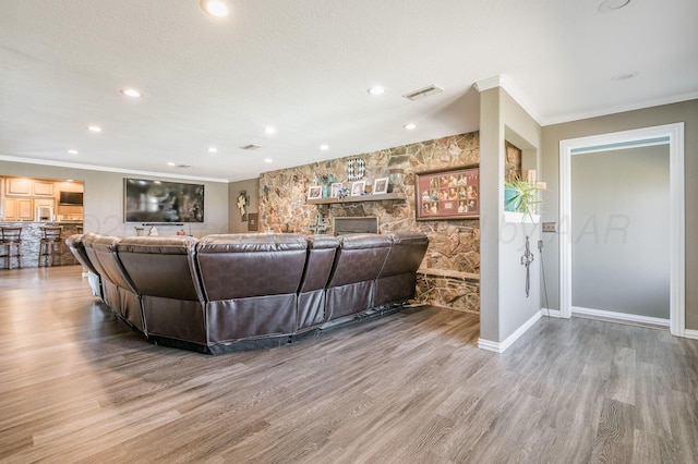 living room with a stone fireplace, ornamental molding, and hardwood / wood-style flooring