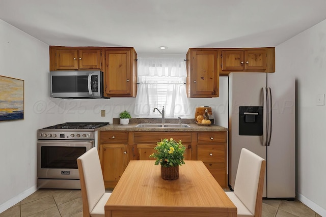 kitchen featuring stainless steel appliances, brown cabinetry, a sink, and light tile patterned floors