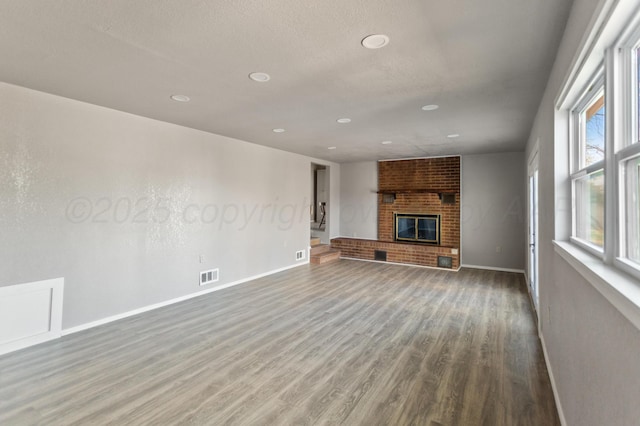 unfurnished living room featuring baseboards, visible vents, a brick fireplace, and wood finished floors